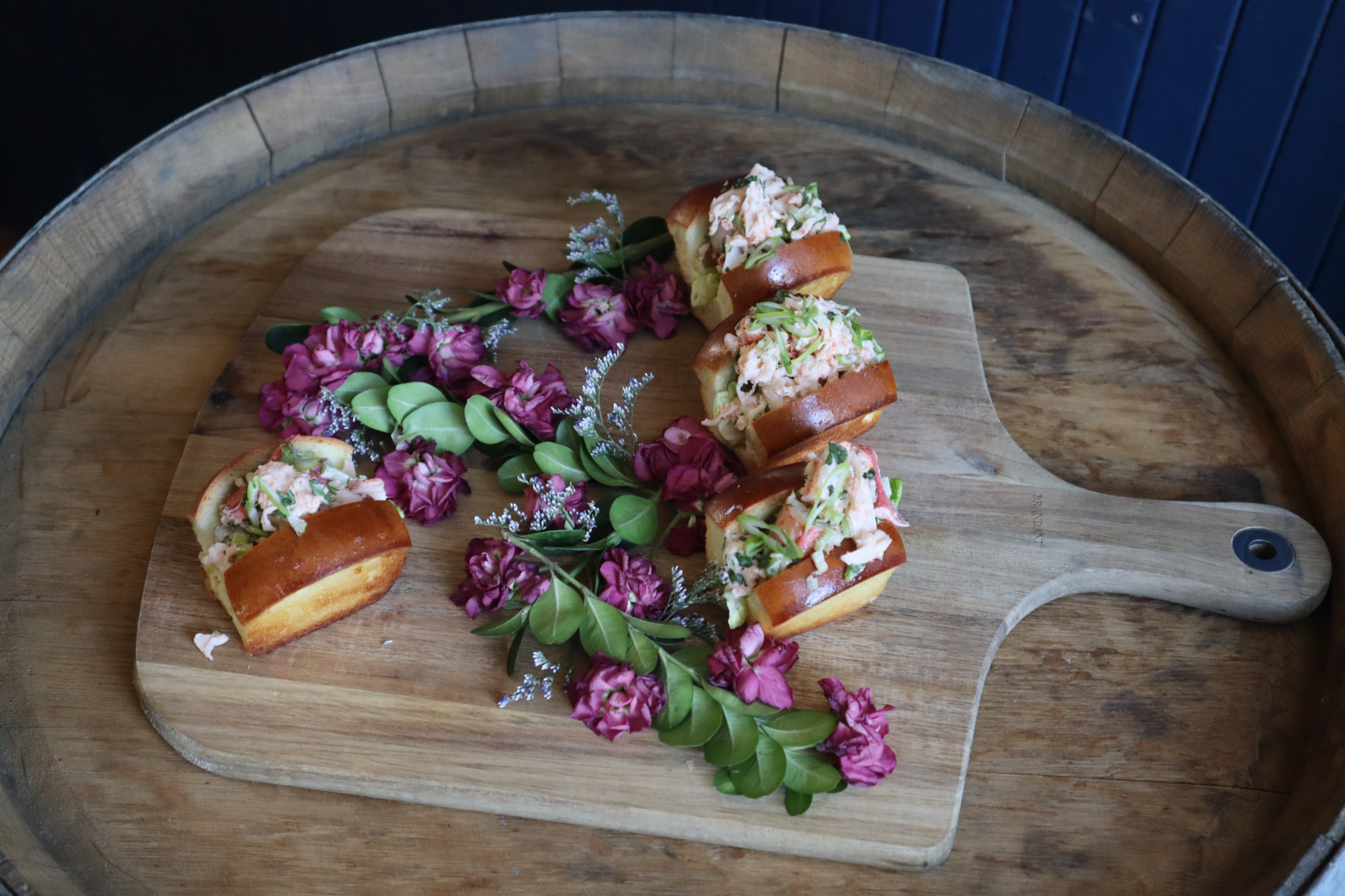 A wooden platter with mini lobster rolls on top of it from JBCE in Boston.