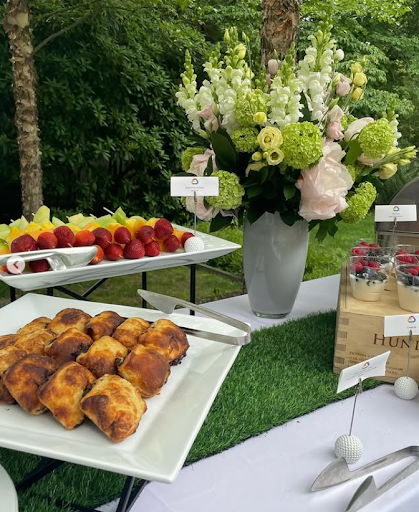 A garden party spread with fresh fruit, pastries, and a floral arrangement in a vase.