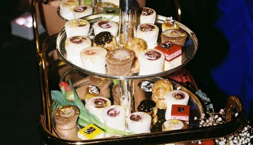 A luxurious tiered dessert display with colorful pastries, surrounded by roses and floral accents.