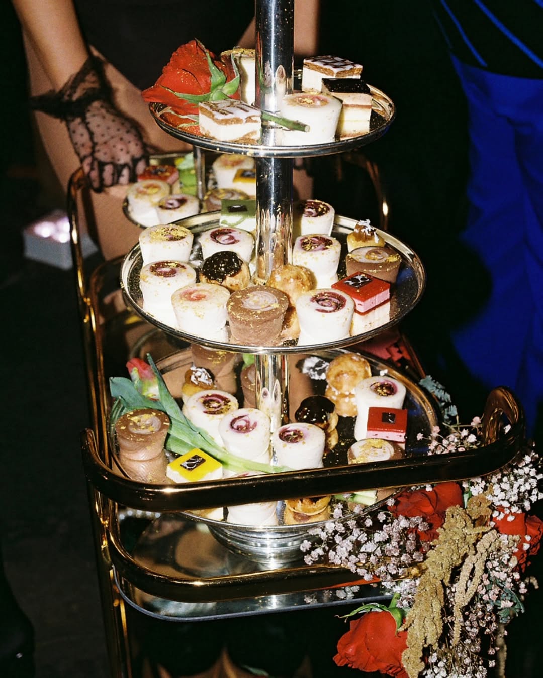 A luxurious tiered dessert display with colorful pastries, surrounded by roses and floral accents.