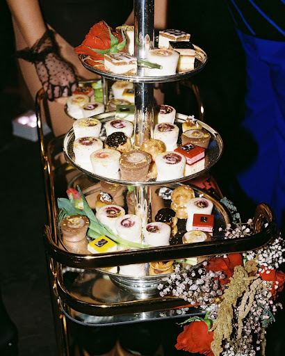 Tiered dessert display featuring colorful macarons, mini cakes, pastries, and rolled sweets arranged for a catered event dessert station.