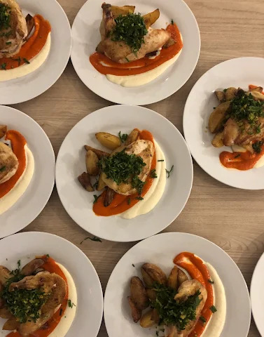 Johnny Burke Catering & Events plated chicken entrées with roasted potatoes, greens, and red pepper sauce.